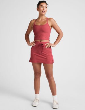 red high-waisted mini athletic skirt with a drawstring at waistband and built-in shorts with pockets.