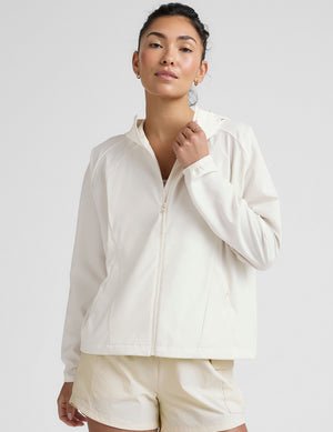 model wearing a white zip-up jacket with hood and shorts on a plain background.